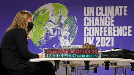 A delegate sits on a table that has an installation showing the 'Climate Clock' inside the venue of the COP26 