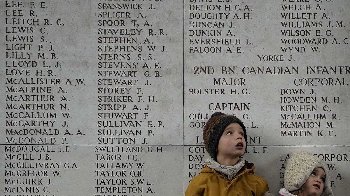Two children look up at a wall of the missing during an Armistice Day ceremony at the Menin Gate Memorial to the Missing in Ypres, Belgium, Thursday, Nov. 11, 2021. 