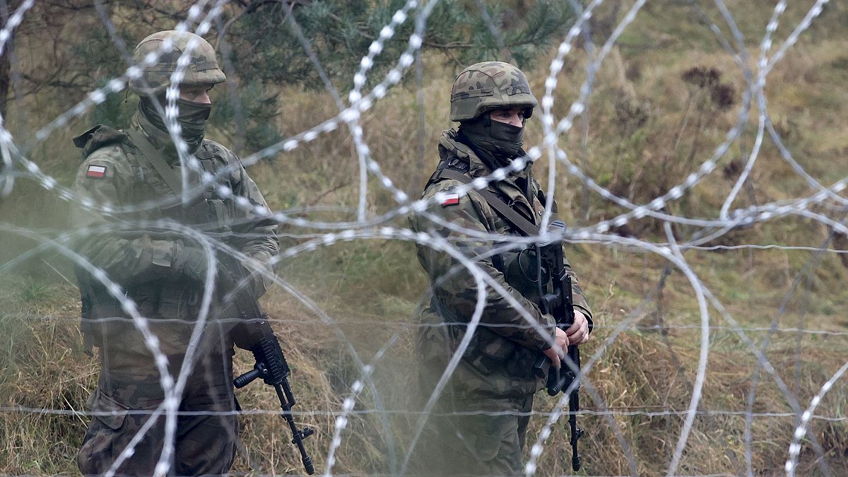 حرس حدود بولنديون يقفون بالقرب من أسلاك شائكة ومهاجرون يتجمعون عند الحدود بين روسيا البيضاء وبولندا. 2021/11/10