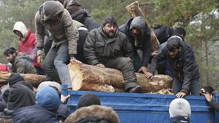 A group of migrants unload a truck with tree trunks delivered by the Belarusian officials in a camp on the Belarusian-Polish border in the Grodno region on November 14, 2021.