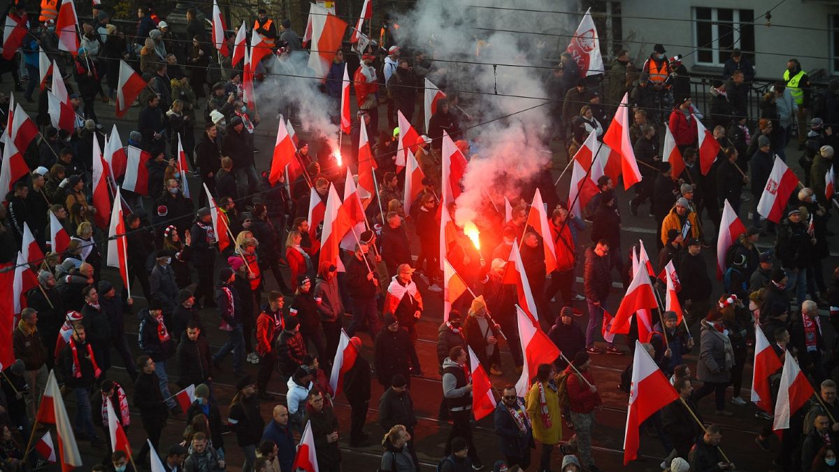 People hold Polish flags, as smoke from flares lit by members of far-right groups rises above the annual Independence Day march in Warsaw, Poland, Nov. 11, 2021.
