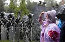 A woman stands at a barbed wire fence in front of a police line toward President Lukashenko's Independence Palace in Minsk, September 2020