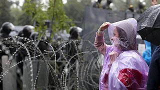 A woman stands at a barbed wire fence in front of a police line toward President Lukashenko's Independence Palace in Minsk, September 2020