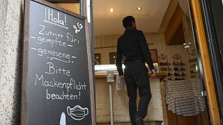 A man enters a Spanish restaurant as he passes a sign reading "Hola! Entry for vaccinated / recovered - Face mask required!" in Stuttgart,Germany