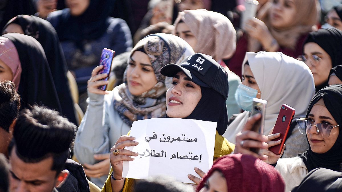 طالبة عراقية ترفع لافتة "مستمرون في اعتصام الطلاب" في احتجاجات مناهضة للحكومة خارج جامعة الكوفة، العراق، 22 ديسمبر 2019