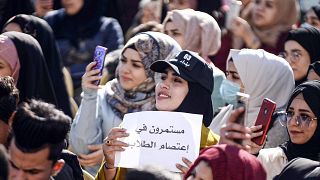 طالبة عراقية ترفع لافتة "مستمرون في اعتصام الطلاب" في احتجاجات مناهضة للحكومة خارج جامعة الكوفة، العراق، 22 ديسمبر 2019