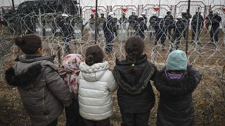 Migrants children stand in front of a barbed wire fence and Polish servicemen at the checkpoint "Kuznitsa" at the Belarus-Poland border, Belarus, Nov. 17, 2021.