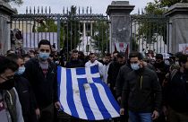 University students stand outside of the Athens Polytechnic and hold a blood-stained Greek flag from the deadly 1973 student uprising during a rally in Athens, Nov. 17, 2021.
