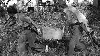 Dos soldados territoriales serbios corren con una caja de granadas capturada en las afueras de la ciudad de Vukovar, Croacia, el viernes 27 de septiembre de 1991