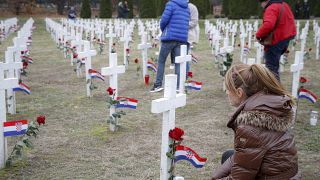 A woman kneels as people lay flowers at Vukovar's memorial cemetery
