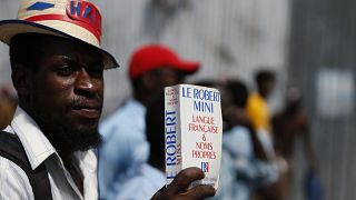 A man carries a paperback French dictionary "Le Robert Mini".