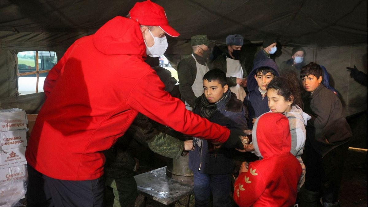 یک کارمند صلیب سرخ بلاروس میان کودکان مهاجر غذا پخش می‌کند