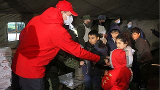 یک کارمند صلیب سرخ بلاروس میان کودکان مهاجر غذا پخش می‌کند