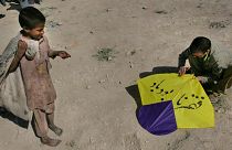 یک پسر فقیر افغان، به تماشای مردی  ایستاده  که مشغول آماده کردن  بادبادکی برای پرواز است؛ بر روی آن نوشته شده «فقر نابود باد»