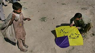یک پسر فقیر افغان، به تماشای مردی  ایستاده  که مشغول آماده کردن  بادبادکی برای پرواز است؛ بر روی آن نوشته شده «فقر نابود باد» 