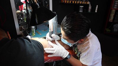 الصبي براندون بورغوس يوشم ذراع أحد العملاء بعناية في استوديو والده في المكسيك.