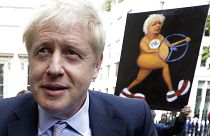 Boris Johnson walks past a satirical art work held up by artist Kaya Mar as he arrives to launch his leadership campaign, in London, Wednesday June 12, 2019