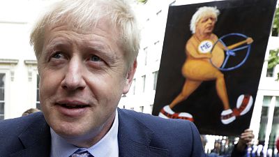 Boris Johnson walks past a satirical art work held up by artist Kaya Mar as he arrives to launch his leadership campaign, in London, Wednesday June 12, 2019