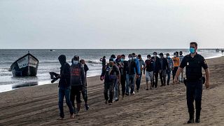 مهاجرون من المغرب يسيرون على طول الشاطئ برفقة الشرطة الإسبانية بعد وصولهم إلى ساحل جزيرة الكناري، الثلاثاء 20 أكتوبر/تشرين الأول 2020