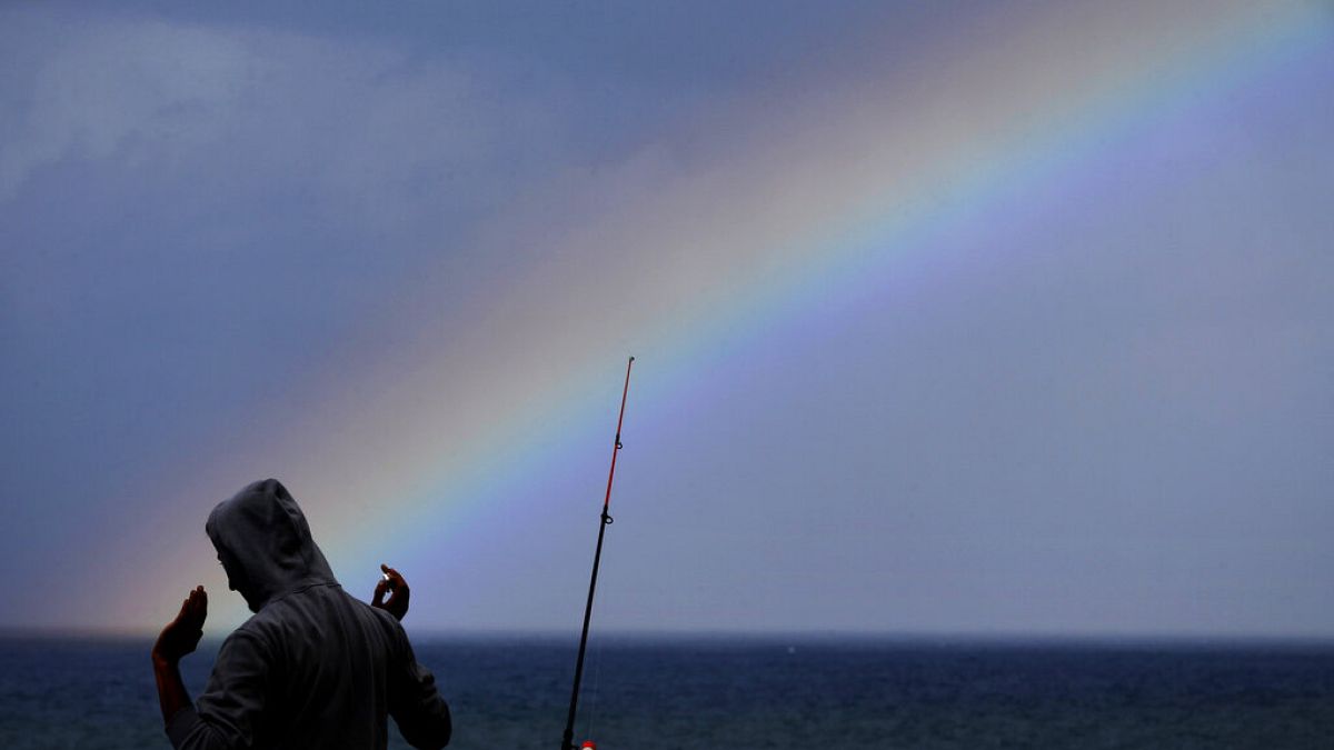 A fisherman speaks to a friend as a rainbow appears over the Mediterranean Sea in Beirut, Lebanon, on Sunday, October 17 of this year