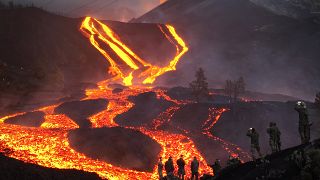 Spanish Army soldiers stand on a hill as lava flows as volcano continues to erupt on the Canary island of La Palma, Spain, Monday, Nov. 29, 2021.
