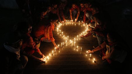 Members of a NGO make a red ribbon, the universal symbol of awareness and support for those living with HIV, with candles on the eve of World AIDS day in India, Nov. 30, 2021.