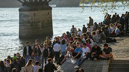 People stroll along the Seine river banks during evening sun in Paris.