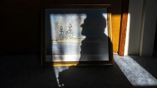 الناجي من بيرل هاربور والمحارب المخضرم في البحرية في الحرب العالمية الثانية ديفيد راسل، يقف لالتقاط صورة مع لوحة يو إس إس أوكلاهوما في منزله. 2021/11/22