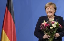 Former Chancellor Angela Merkel laughs as she receives flowers from new elected Chancellor Olaf Scholz during a handover ceremony in the chancellery in Berlin, Dec. 8, 2021.
