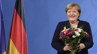 Former Chancellor Angela Merkel laughs as she receives flowers from new elected Chancellor Olaf Scholz during a handover ceremony in the chancellery in Berlin, Dec. 8, 2021.