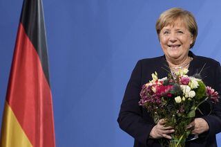 Former Chancellor Angela Merkel laughs as she receives flowers from new elected Chancellor Olaf Scholz during a handover ceremony in the chancellery in Berlin, Dec. 8, 2021.