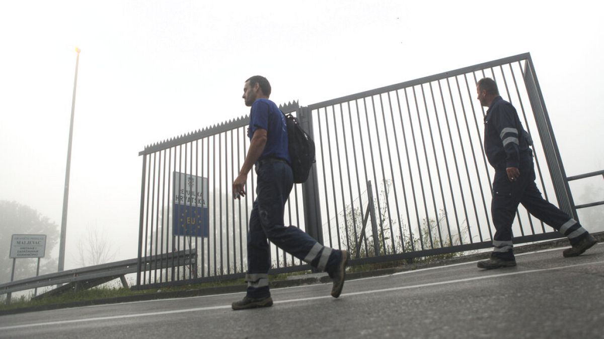 FILE: Two men walk past a section of the fence along the border between Croatia and Bosnia near the village of Maljevac, Croatia, Tuesday June 11, 2019.