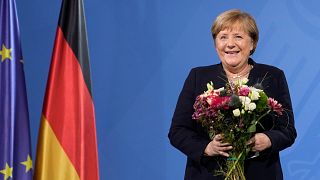 The former Chancellor laughs as she receives flowers from the newly elected Olaf Scholz during a handover ceremony