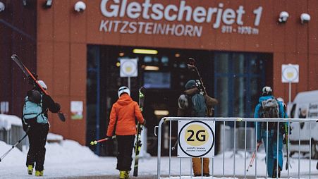 Skiers walk towards the entrance of the valley station Kitzsteinhorns, as a sign indicates the so-called 2G rule in Kaprun near Salzburg, Austria.