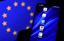Logos of Google, Apple, Facebook, Amazon and Microsoft displayed on a mobile phone with an EU flag in the background