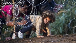 a child is helped cross from Serbia to Hungary through the barbed wire fence near Roszke, southern Hungary