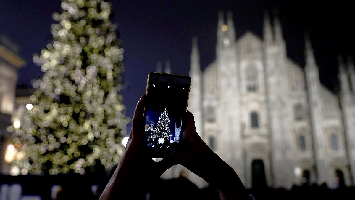 A woman takes pictures of the lit Christmas tree in front of the Duomo gothic cathedral, in Milan, Italy, Sunday, Dec. 16, 2018