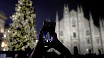 A woman takes pictures of the lit Christmas tree in front of the Duomo gothic cathedral, in Milan, Italy, Sunday, Dec. 16, 2018