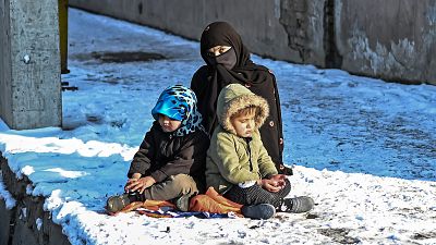 سيدة تجلس مع طفليها على جانب طريق مغطى بالثلوج في كابول