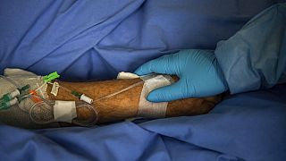 Védőruhába öltözött orvos fogja egy koronavírusos  beteg kezét a Honvédkórházban