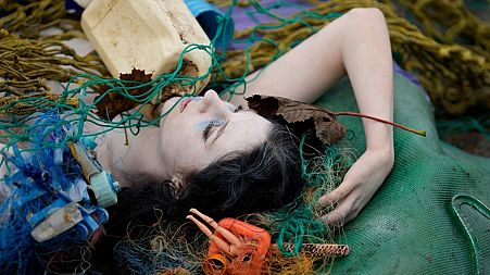 A woman lies amongst plastic waste during an XR protest in Glasgow at COP26, November.