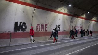 Migrants headed to France from Italy walk past graffiti that reads "No One is Illegal" in a tunnel leading to the French-Italian border, Saturday, Dec. 11, 2021.