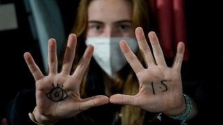A young woman with an eye drawn on her hand to show she is watching and 1.5 for countries to keep warming below 1.5 degrees Celsius.