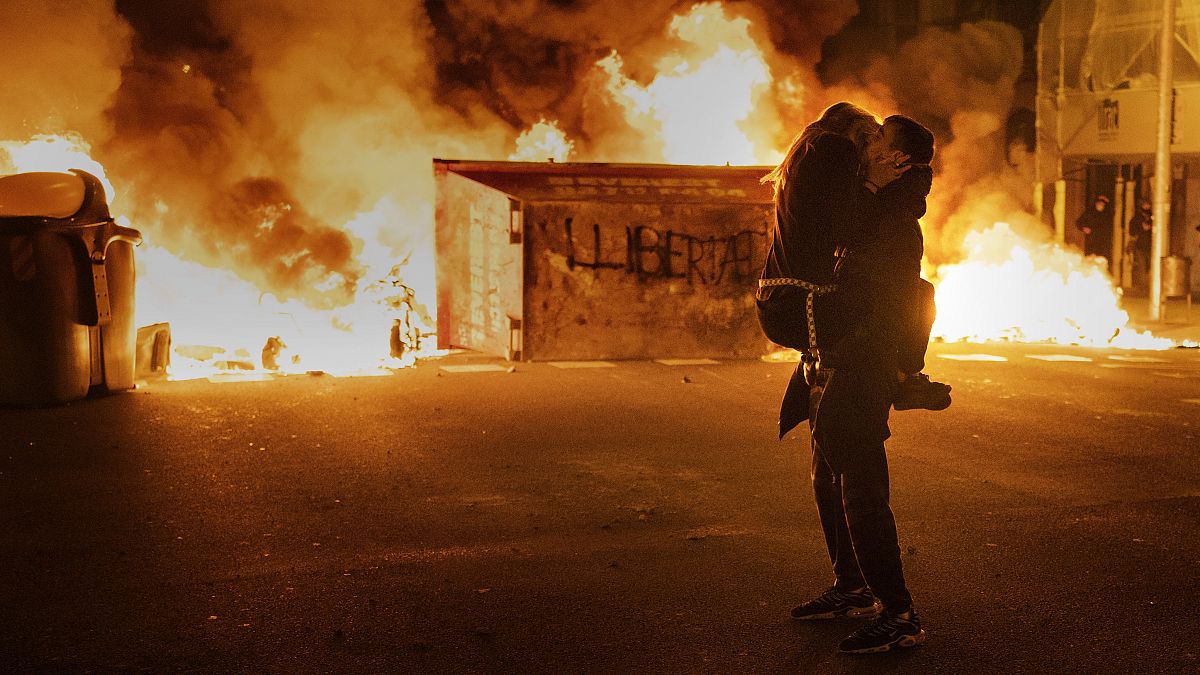 Egy pár csókolozik, miközben a tüntetők rendőrökkel csapnak össze Barcelonában, a Pablo Hasel rapper elítélése utáni demonstráción 2021. február