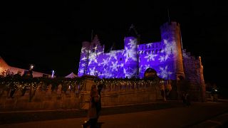 Two people walk by a Christmas projection on the Steen Castle in the historical center of Antwerp, Belgium, Monday, Dec. 20, 2021.