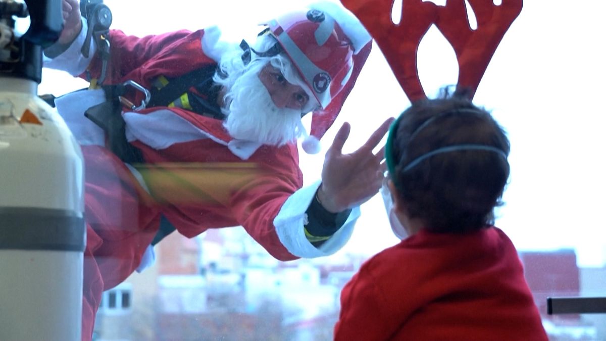 Jordi Valls, dressed as Santa Claus, and another firefighter greeting children inside the hospital while hanging from ropes outside the window 