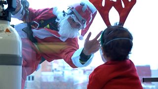 Jordi Valls, dressed as Santa Claus, and another firefighter greeting children inside the hospital while hanging from ropes outside the window