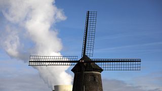 بخار يتصاعد من محطة للطاقة النووية خلف طاحونة هوائية قديمة على نهر شيلدت في دويل، بلجيكا.