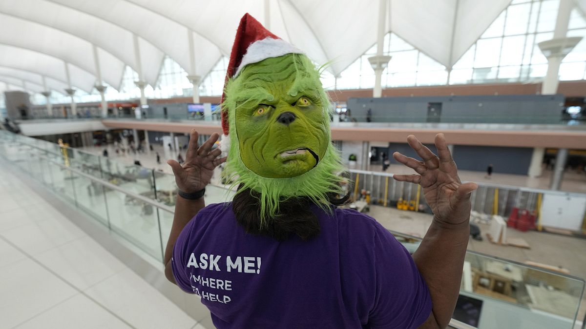 An airport ambassador wears a grinch mask while waiting to help to direct travellers in the terminal of Denver International Airport