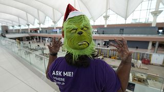 An airport ambassador wears a grinch mask while waiting to help to direct travellers in the terminal of Denver International Airport